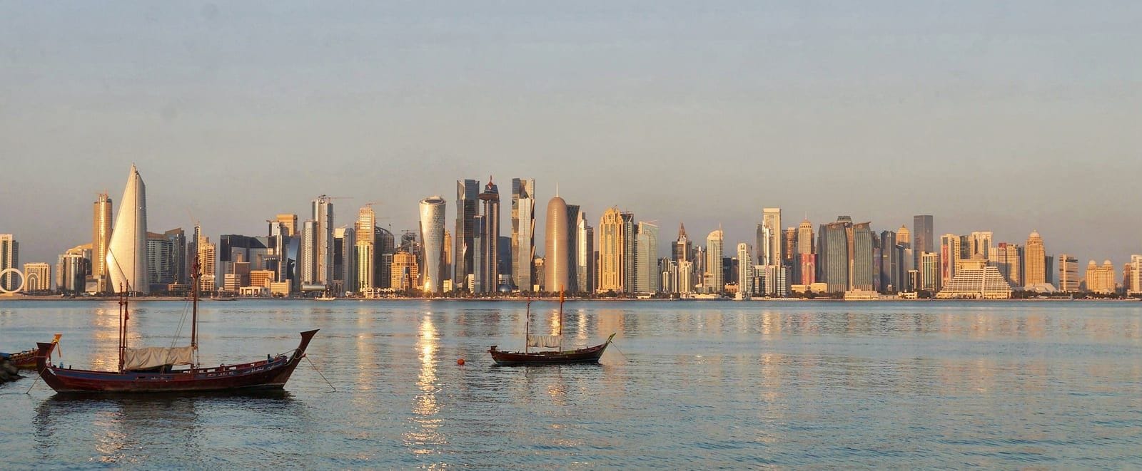 Panorama West Bay odbijająca się w zatoce Doha, sfotografowana z promenady Corniche o zachodzie słońca.